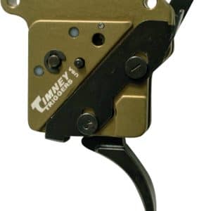 Close-up of a Timney Triggers firearm trigger mechanism with a gold-colored housing and black lever/hammer, showing screws and adjustment components.