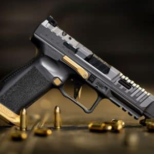 Close-up of a black and gold semi-automatic handgun resting on a wooden surface, with brass cartridges scattered around.