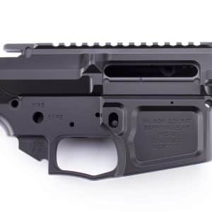 Close-up of a black AR-style rifle receiver showing a Picatinny rail on the upper, ejection port area, and safety markings on the lower receiver.