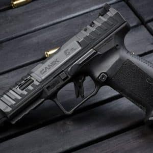 Semi-automatic handgun with a textured grip on a dark wooden surface, with spent shell casings nearby.