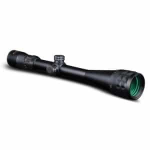 Black rifle scope with adjustable knobs and a green-tinted lens on a white background.