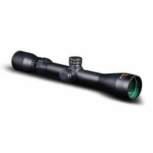 Black riflescope with adjustment turrets and a green-tinted objective lens, angled to show side and eyepiece details at rest on a white background.