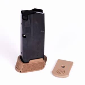 A dark handgun magazine standing upright in a tan pistol grip with the base plate detached nearby on a white background.