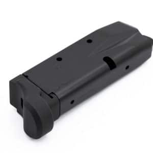 Black pistol magazine lying on a white surface, angled with a textured base plate visible.