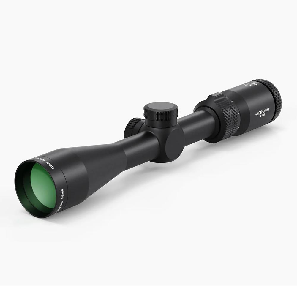 Black riflescope with green-tinted front lens and two adjustment knobs on a white background.