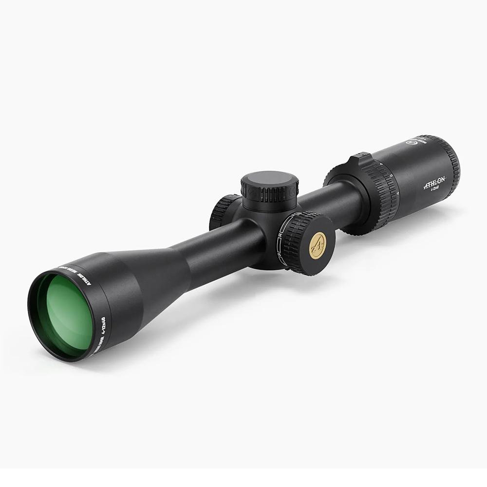 Black riflescope with green-tinted objective lens, centered adjustment turrets, and knurled eyepiece shown at an angle on a white background